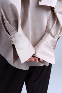 The beige caped shirt Diva is a unique creation that blends classic elegance with a modern twist. This button-down shirt features a cape-like design that gracefully drapes over the shoulders and back, creating a stunning winged effect. The puffy long sleeves with bell-shaped cuffs add a touch of refinement to this exquisite piece. Crafted from premium cotton satin, the Diva Beige shirt is not only luxurious but also comfortable to wear all day long. Its adaptable design allows you to experiment Button Clothes Design, Shirt Cuffs Design, Sleeve Cuffs Ideas, Unique Button Up Shirts, Bottom Down Shirt Outfits, Cuff Design Sleeve, Shirt Cuff Styles, Cuff Sleeves Design, Unique Sleeves Design