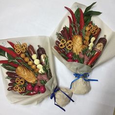 two wrapped bouquets filled with different types of vegetables and pretzels on white paper