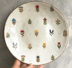 a hand is holding a white plate with colorful flowers on it's sides and the bottom