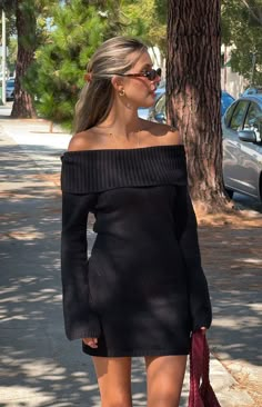 a woman is walking down the street in a black dress