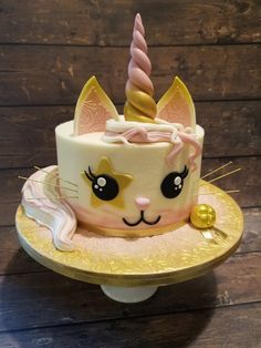 a cake with a cat face and unicorn horn on it's head is sitting on a gold plate