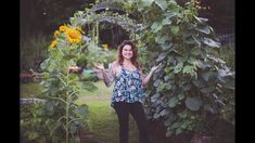 a woman standing in front of a sunflower arch with her hands out to the side