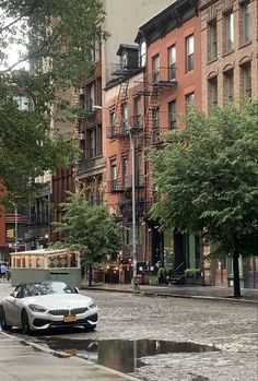 a car parked on the side of a wet street next to tall buildings and trees