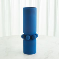 a tall blue vase sitting on top of a white table next to a curtained window