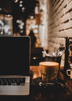 a laptop computer sitting on top of a wooden table next to a cup of coffee