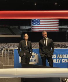 two men in suits standing next to an empty bleachers with the american flag behind them