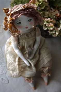 a doll is sitting next to a potted plant on a white cloth tablecloth