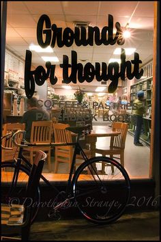 there is a bicycle parked in front of the store's glass window that says, grounds for thought