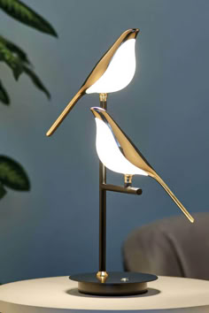 a table lamp that has two birds on it and one is turned on to look like they are touching each other