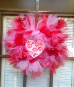 a heart shaped wreath hanging on the side of a window with red and pink tulle