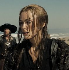 a woman with long hair standing next to a man in pirate costume on the beach