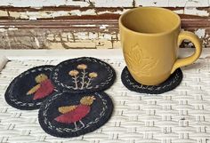 three coasters with embroidered designs on them next to a coffee cup and saucer