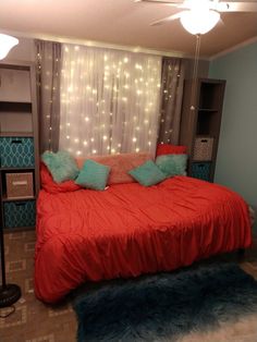 a bed with red sheets and blue pillows in a room decorated with christmas lights on the wall