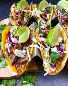 several tacos with meat and vegetables on a cutting board next to lime wedges