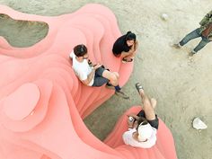 three people sitting on pink couches in the sand