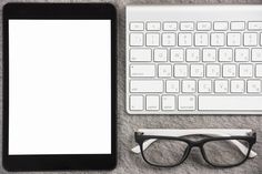 a tablet, glasses and keyboard on a gray carpet