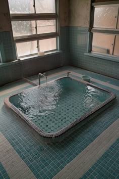 an empty bathtub in a bathroom with blue tiles on the floor and windows above it