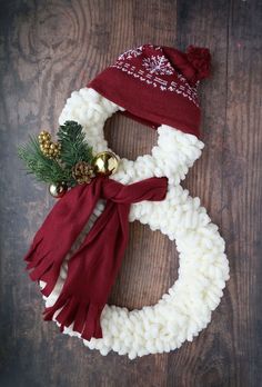 a knitted snowman wreath with bells and pineconis on the top, sitting on a wooden surface