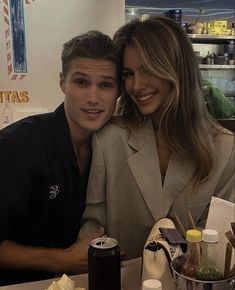 a man and woman sitting at a table with food in front of them, posing for the camera