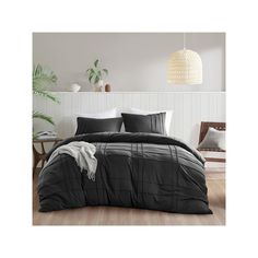 a bed with black comforter and pillows in a room next to a plant on the wall