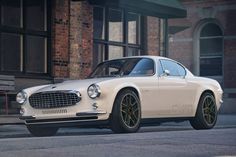 an old fashioned white car parked on the side of the road in front of a brick building