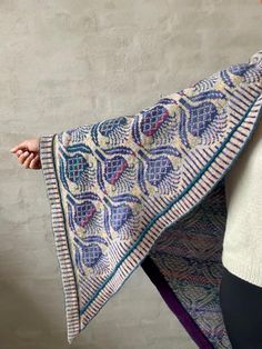 a woman is holding up a blue and white shawl with an intricate design on it