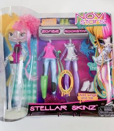 two dolls in plastic packaging on a white surface, one is pink and the other is green