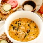 a white bowl filled with soup sitting on top of a plate next to crackers and cucumbers