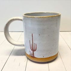 a white coffee mug with a cactus design on the outside and inside, sitting on a wooden floor