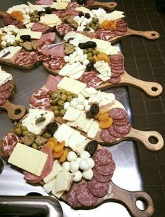 an assortment of meats, cheese and olives on a metal tray with wooden spoons