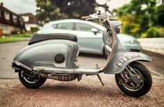 an old scooter is parked on the side of the road next to a car