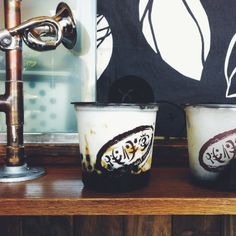 two cups sitting next to each other on a wooden shelf with a faucet