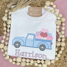 a white shirt with a blue truck and heart balloons on the back is next to some wood beads