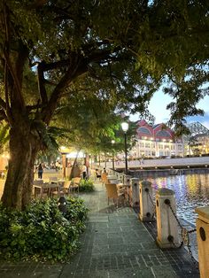 people are sitting at tables by the water in front of some buildings and trees with lights on them