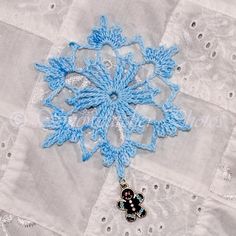 a blue snowflake is hanging on a white quilted piece of fabric with silver sequins