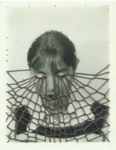 an old black and white photo of a woman covering her face behind a piece of wire