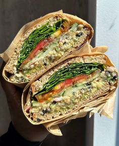 two sandwiches with different toppings are held in brown paper wrappers on a white wall