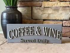 a sign that says coffee and wine served daily on a table next to a potted plant