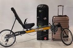 a yellow bicycle parked next to two suitcases and a bike with a seat on it