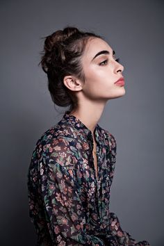 a woman with her hair in a bun is posing for the camera, wearing a floral shirt