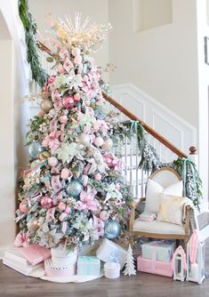 a decorated christmas tree sitting in the middle of a living room next to a stair case