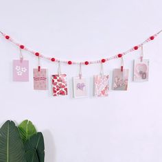 some pictures hanging from a string on a white wall next to a potted plant