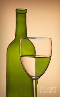 a wine glass and bottle sitting next to each other in front of a beige background