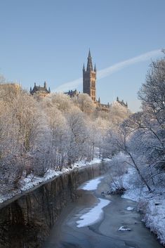 a river running through a snow covered forest next to a tall building on top of a hill