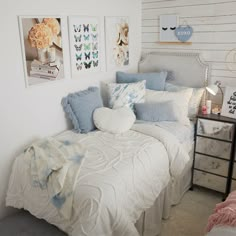 a bed with blue and white pillows on top of it next to pictures hanging on the wall