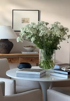 a vase filled with white flowers sitting on top of a table next to two chairs