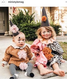 two children dressed up as clowns sitting on the ground in front of a house