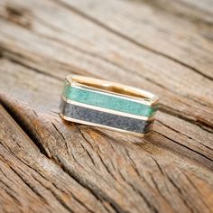 a gold and green ring sitting on top of a piece of wooden planked surface