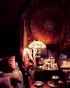 a room with a table, lamp and tapestry hanging on the wall above it's head