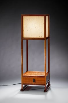 a wooden stand with a lamp on top and a cord attached to the side, in front of a gray background